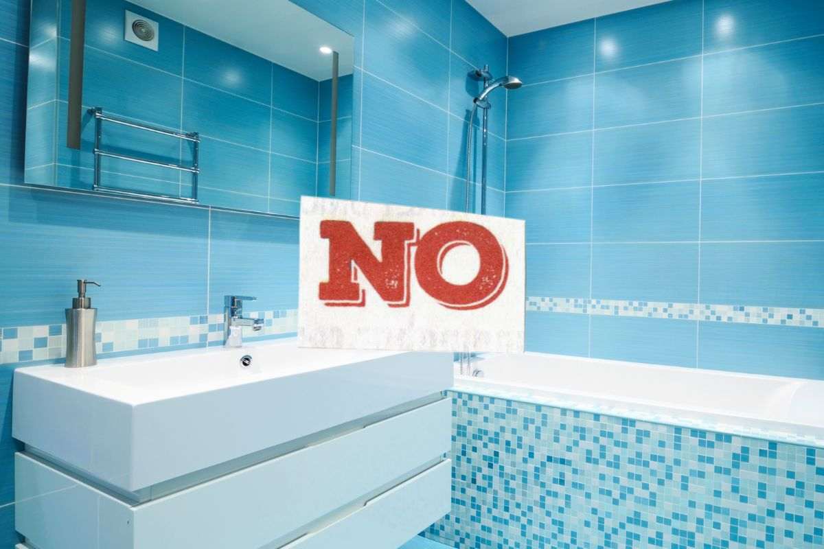 bagno con piastrelle azzurre con vasca e lavandino e scritta no