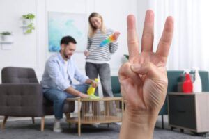sfondo in cui si vedono dei ragazzi che riordinano casa e in primo piano una mano che fa numero 3